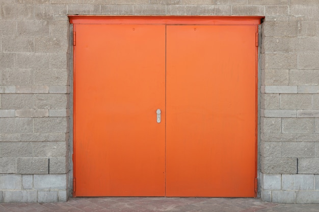 Front view of wide orange or bright red door set in gray stone brick wall with edging