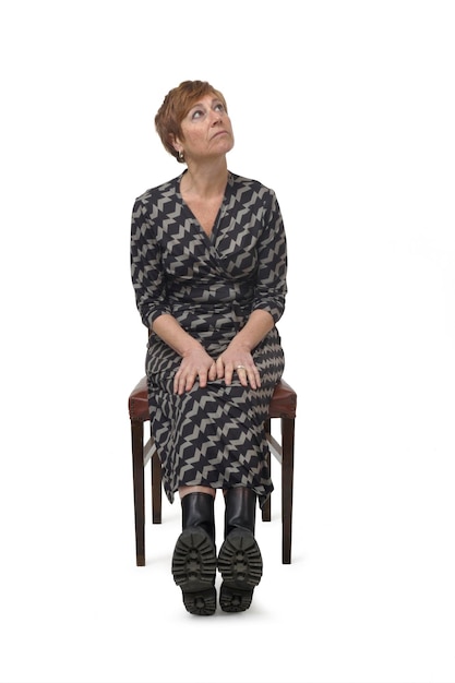 Front view a woman in dress and boots sitting on chair looking up on white background