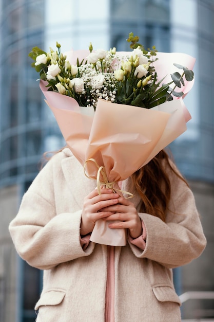 Photo front view of woman holding bouquet of flowers in front of her face outdoors