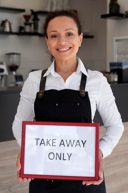 Front view of woman wearing apron holding sign with takeaway only