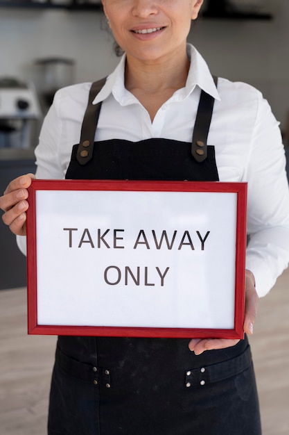 Front view of woman wearing apron holding sign with takeaway only