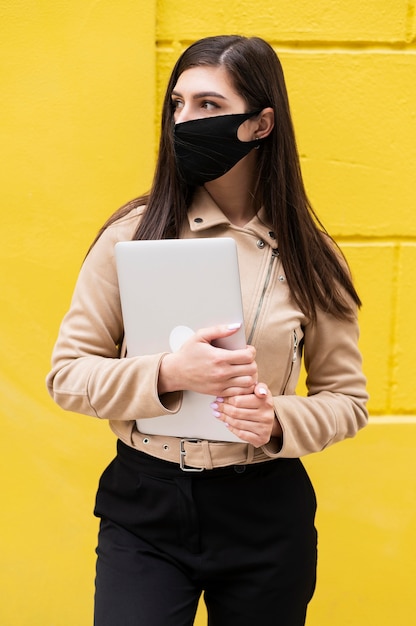 Front view of woman with face mask holding laptop