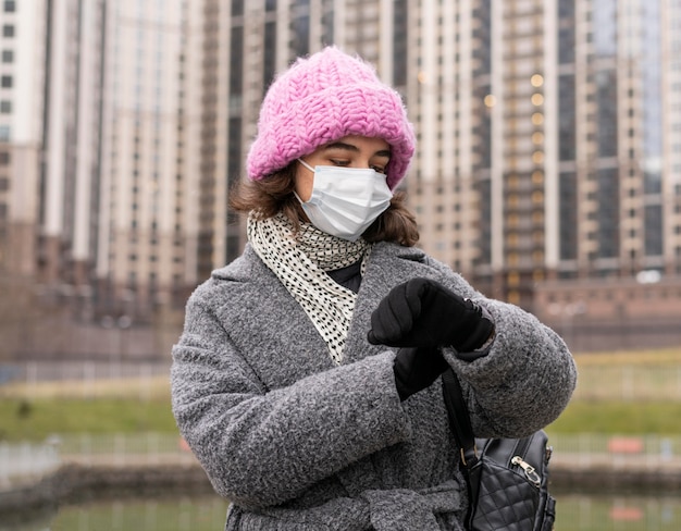 Front view of woman with medical mask in the city looking at watch