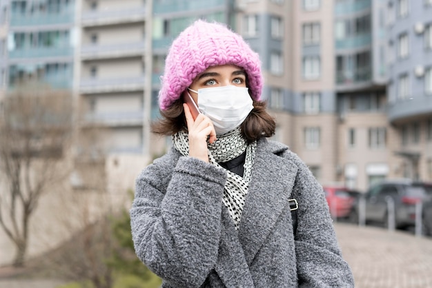 Front view of woman with medical mask in the city talking on smartphone