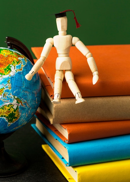 Photo front view of wooden figurine with academic cap on books and globe