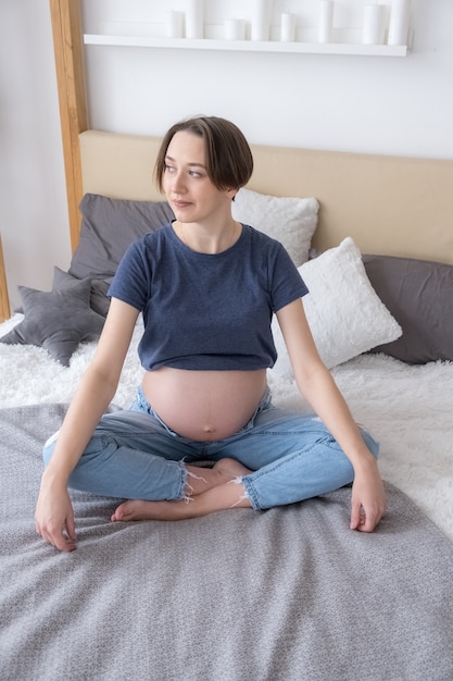 Front view of young adult pregnant woman sitting in bed in lotus position practicing meditation, concept HLS, yoga