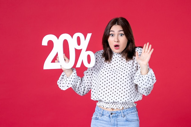 Front view of young female posing with discount on red wall