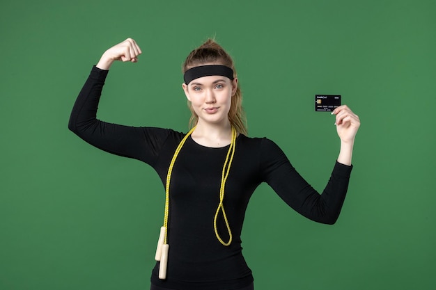 Front view young female in sport clothing holding bank card on green background workout body flex health athlete woman money