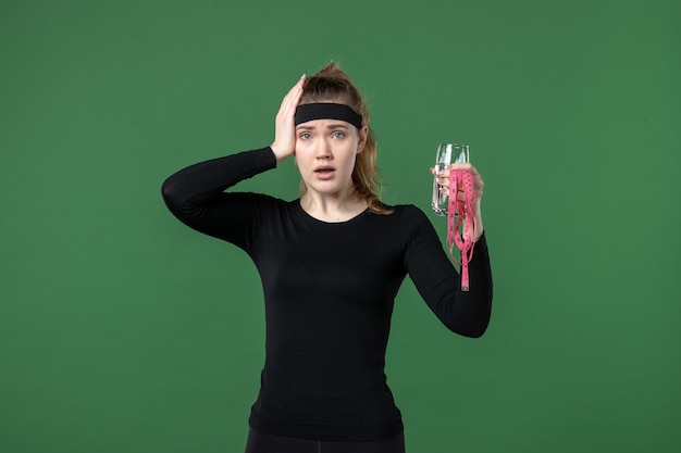 Front view young female with glass of water and waist measure on green background health sport athlete body black workout woman