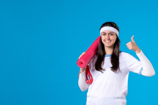 Front view young female with yoga mat on blue wall