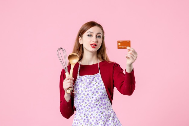 front view young housewife holding whisk and bank card on pink background kitchen pie cake woman color shopping cooking money food