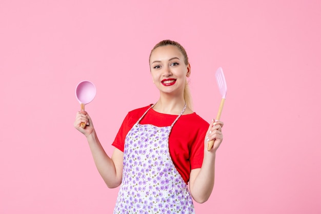 Front view young housewife posing with cutlery on pink wall