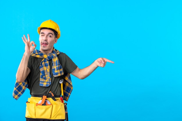 front view young male builder in yellow helmet on blue background constructor architecture building color tool worker