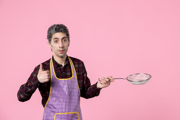 front view young male in cape holding sieve on pink background cook job profession husband kitchen horizontal food worker colors