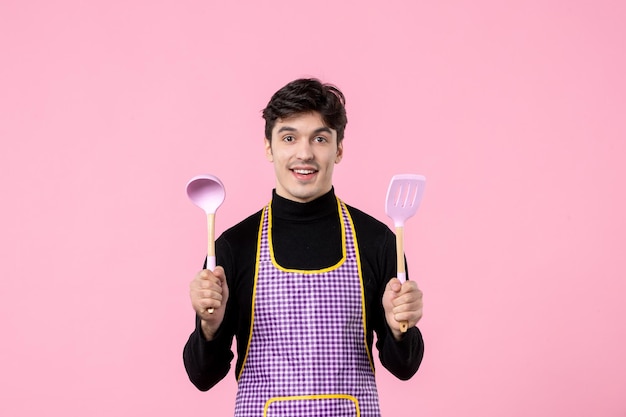 Front view young male in cape with spoons on pink background color food cooking profession uniform work dough cuisine