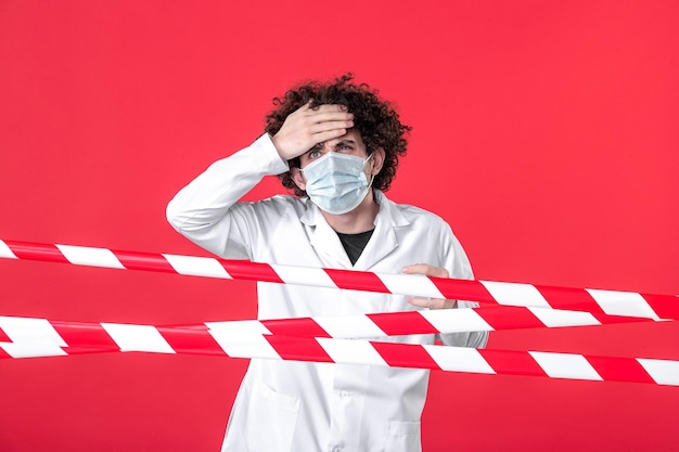 Front view young male doctor in medical uniform and mask on red background isolation hospital covid- health quarantine danger strip