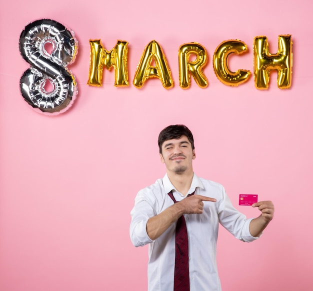 Front view young male holding pink bank card with march decoration on pink background color money party holiday feminine equality shopping man present