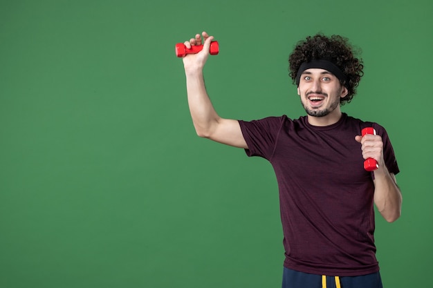 front view young male holding red dumbbells on green background sport gym emotion health model workout athlete lifestyle run color