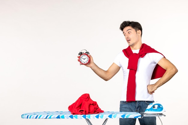 Front view young male behind ironing board holding clocks on white background laundry work housework clean emotion time man color