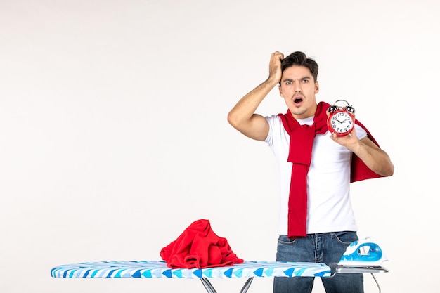 Front view young male behind ironing board holding clocks on white background man laundry home work clean emotion time color