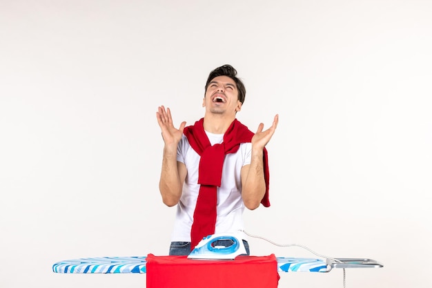 Front view young male ironing towel and laughing on white surface