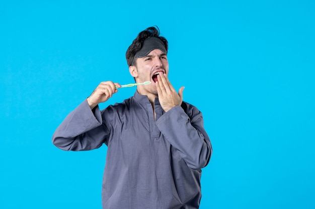 front view young male in pajamas holding toothbrush and yawning on blue background nightmare bed night color rest human wake clean dream