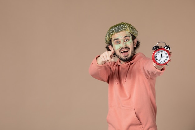 front view young male with mask holding clocks on brown background time spa therapy salon bodycare facial