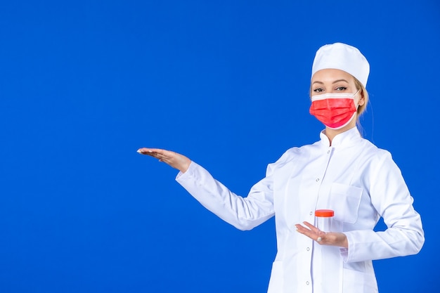 front view young nurse in medical suit with mask holding flask on blue background hospital virus covid- doctor health medicine pandemic vaccine