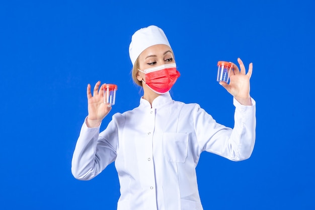 front view young nurse in medical suit with red mask holding flasks on blue background drug health doctor covid- pandemic hospital virus