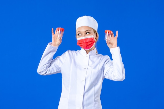 front view young nurse in medical suit with red mask holding flasks on blue background health virus covid- hospital drug doctor pandemic