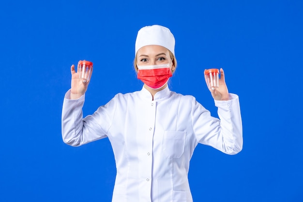 front view young nurse in medical suit with red mask holding flasks on blue background health virus pandemic covid- medicine drug doctor