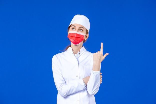 Front view young nurse in medical suit with red protective mask on blue wall