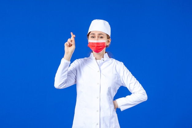 Front view young nurse in medical suit with red protective mask on blue wall