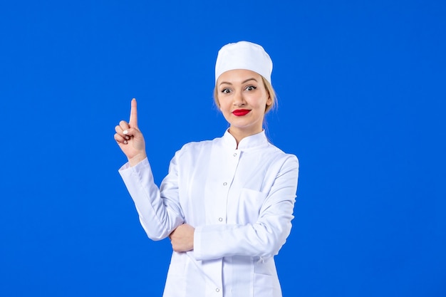 front view of young nurse in white medical suit on blue wall