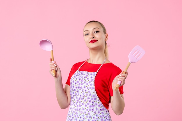 Front view young pretty housewife in cape with spoons on pink wall