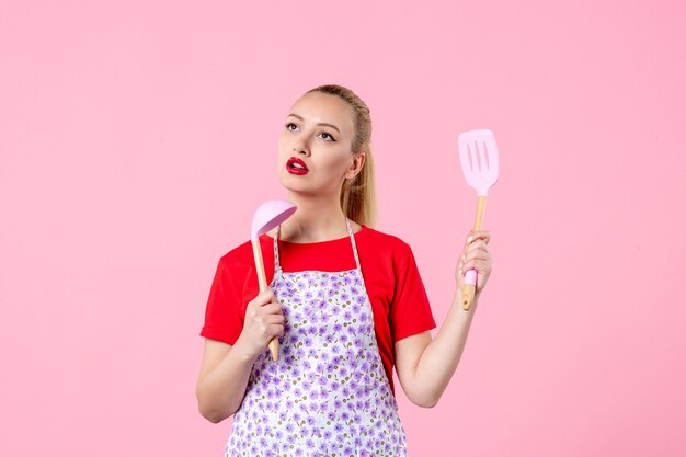 Front view young pretty housewife in cape with spoons on pink wall