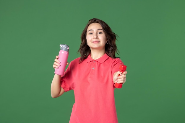 Front view young saleswoman holding thermos and dumbbell on green background color yoga uniform job athlete shopping body work