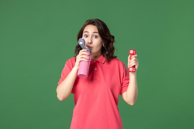 Front view young saleswoman holding thermos and dumbbell on green background job color yoga uniform athlete shopping workout body work