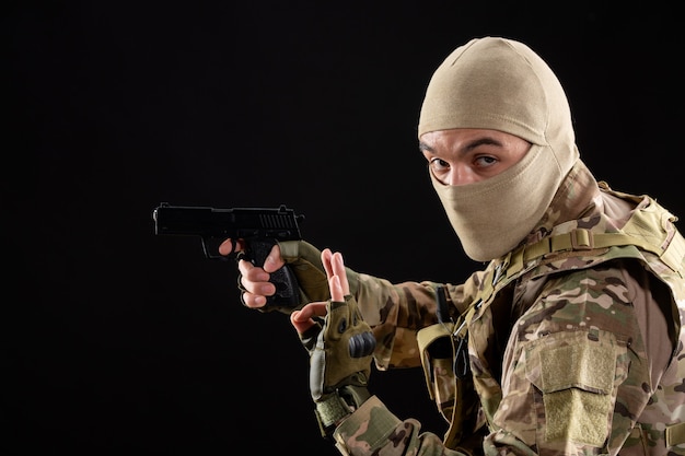 Front view young soldier in uniform aiming gun on black wall