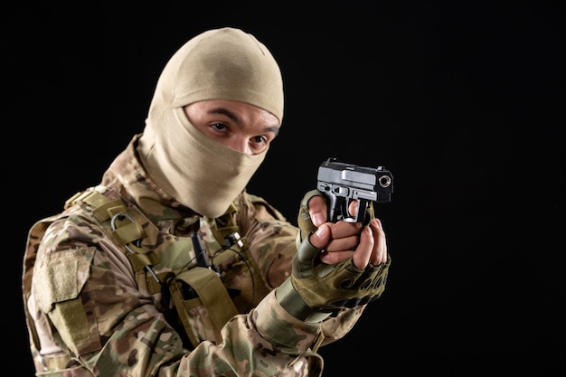 Front view of young soldier in uniform aiming gun on black wall