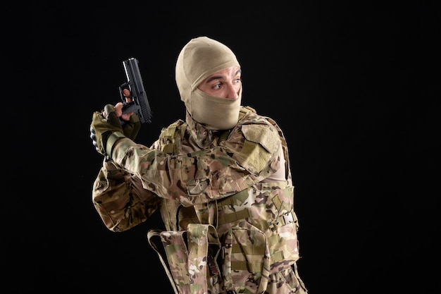 Front view young soldier in uniform with gun black wall