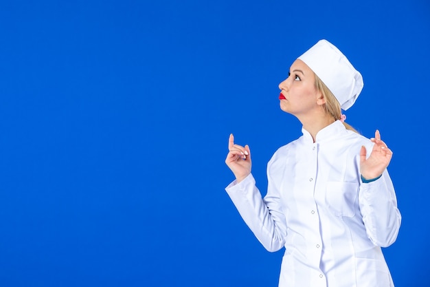 front view of young thinking nurse in medical suit on blue wall