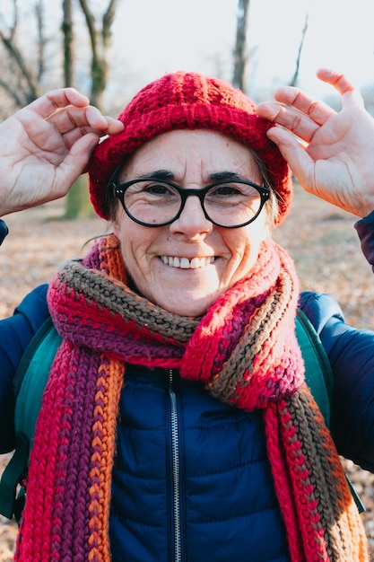 Frontal portrait of an old woman smiling to camera using glasses and putting on a cap for the cold and winter Aging well and healthy concept family grandmother image Active third age concept