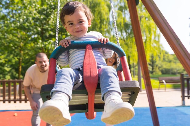 Frontal view of parents swinging a small child at the playground in a sunny day