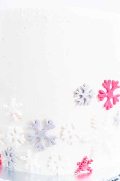 Frosting a tall round cake with white Italian buttercream icing and decorating with fondant snowflakes.