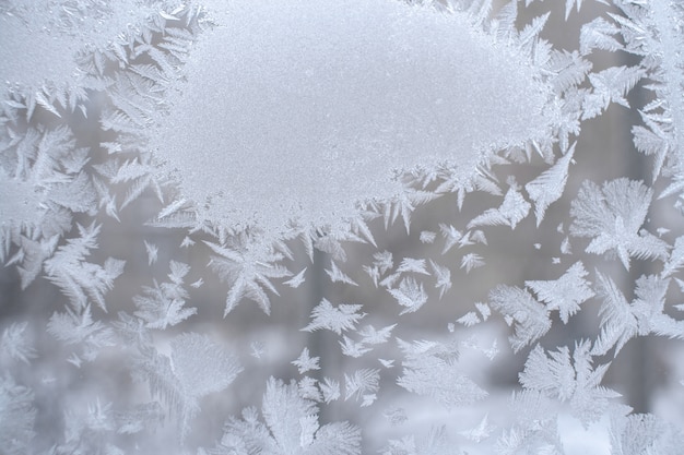 Frosty pattern in form of spot and beautiful pointed snowflakes around it on winter window pane.