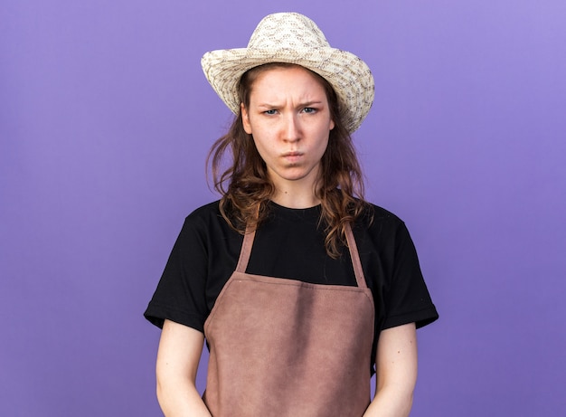 Frowning looking camera young female gardener wearing gardening hat 