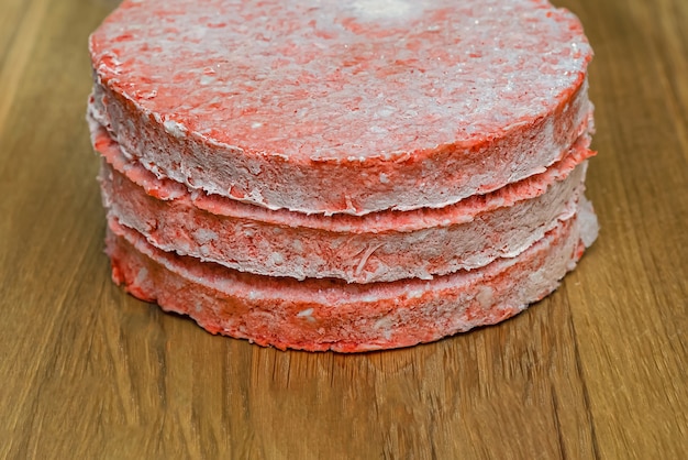 Frozen beef burger patties are placed on a wooden cutting board before cooking. Freezing in the freezer.