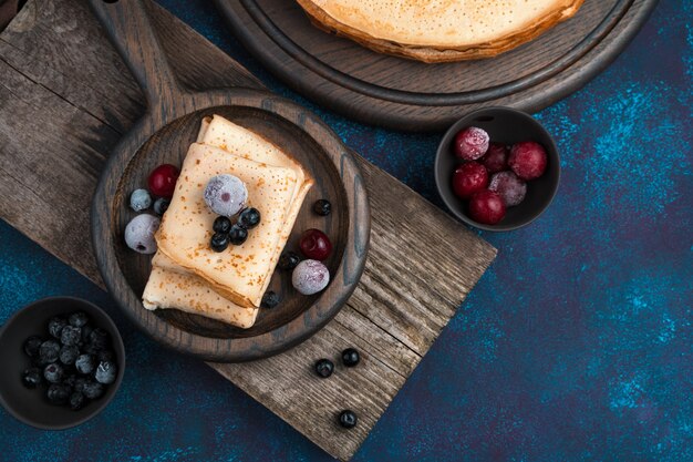 Frozen berries on fried pancakes on a dark blue background.