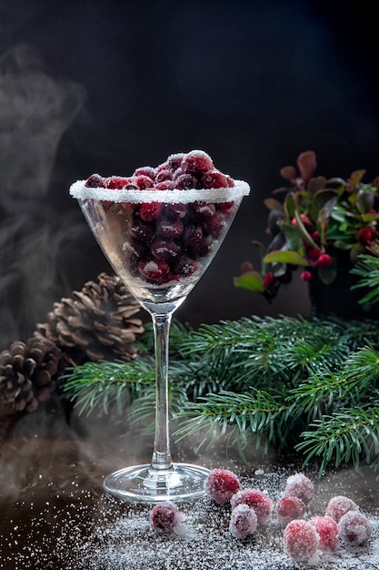 Frozen cranberries in sugar in a cocktail glass on a table decorated with Christmas tree branches and cones